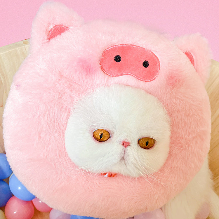 White cat wearing a pink pig plush pet neck warmer